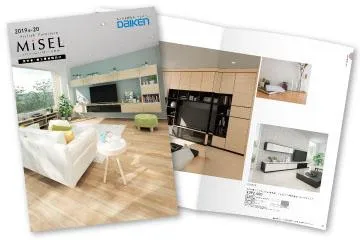 大建工業「MiSEL」のカタログ表紙画像。画像には木目フローリングを使用したリビングが写っており、右側にはカタログにはテレビボード、本棚・飾り棚、天袋が一体になったハイタイプのオーダーテレビ壁面収納が置かれている。壁面収納の引出しの扉はホワイトアッシュの木目で、取っ手はついていない。扉の中には本やテレビ、AV、観葉植物が置かれている。画像の左にはソファやデスクがある。日差しが差し込み明るい室内が表現されている。